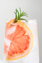 Close up of glass of cold water with grapefruit and rosemary garnish.