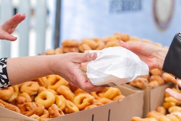 Woman's hands selling doughnuts rolled in paper for sale with doughnuts in bulk, food concept.
