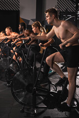 Fototapeta na wymiar strong men and women riding an exercise bike, people exercising on stationary bike together, concentrated on cardio training