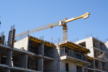Construction site. Facade structure of a building under construction. Yellow construction crane behind the building against the blue sky.