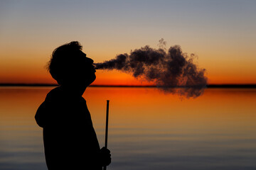 Fototapeta premium Exhales smoke at sunset. Smoking hookah.