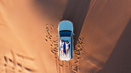 AERIAL. Top view of young couple relaxing on the car's roof at the desert.