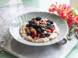 Delicious breakfast oat porridge on plant milk with nuts and berries on marble table