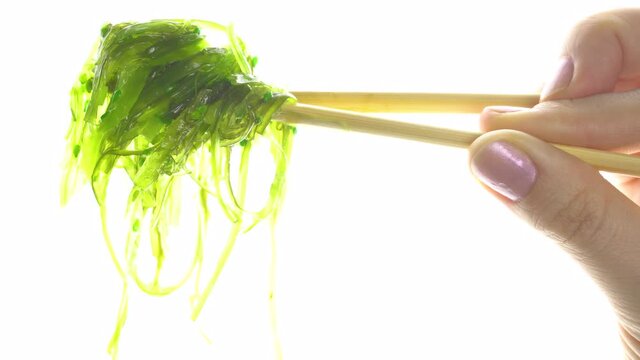 Female hand holding chuka seaweed with chopsticks on a white background.Close-up.