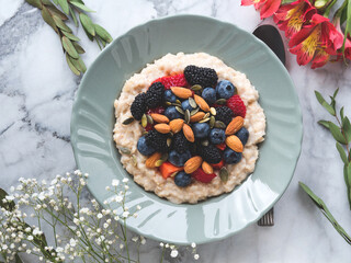 Delicious breakfast oat porridge on plant milk with nuts and berries on marble table
