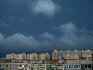 Sunrise at the residential area of the Cheboksary city with dark blue storm sky and clouds, sun rays and buildings.