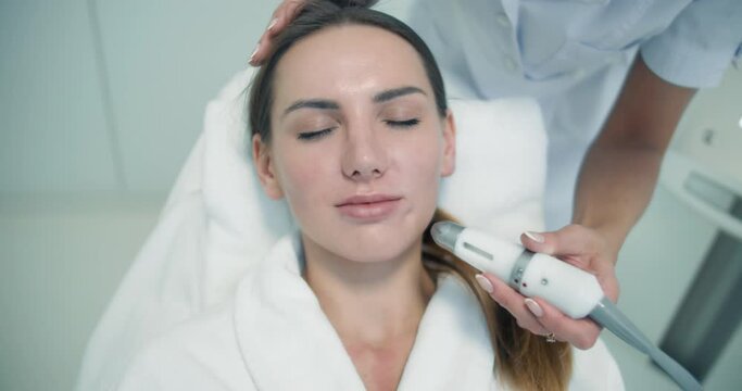 Close-up face of a female client in a bathrobe is having a non-injection bio-revitalization procedure on her cheek and under the nose by using the Dermadrop TDA device.