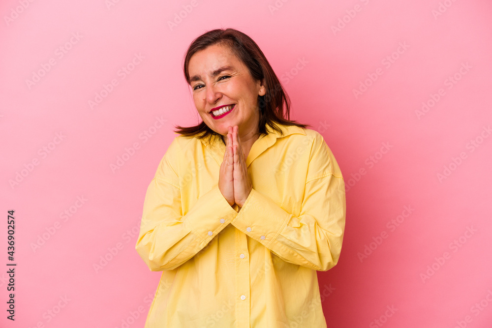 Wall mural middle age caucasian woman isolated on pink background holding hands in pray near mouth, feels confi