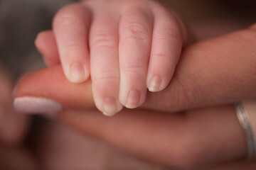 A newborn holds on to mom's, dad's finger. Hands of parents and baby close up. A child trusts and holds her tight. 