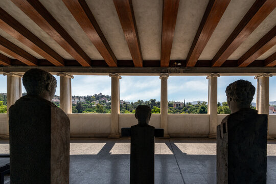 Athens, Attica, Greece. Ancient statues in male figure at the Stoa of Attalus admiring the view of the archaeological site of the Ancient Agora of Athens, Temple of Hephaestus