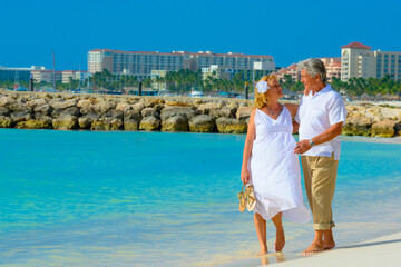 Fototapeta na wymiar Older couple hugging and walking on the beach in white outfits in Aruba, Caribbean