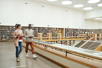 Blurred motion of people walking along the corridor in big library - Powered by Adobe