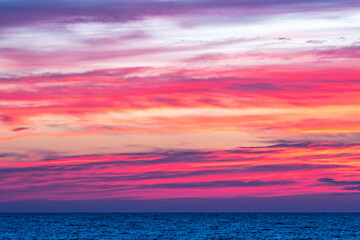 Naklejka na ściany i meble Dramatic pink purple sky at dusk over ocean at sunset