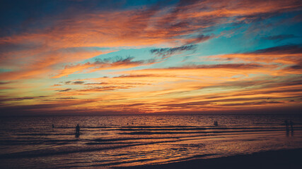 Fototapeta na wymiar Vibrant sunset sky reflected in water as people enjoy the ocean