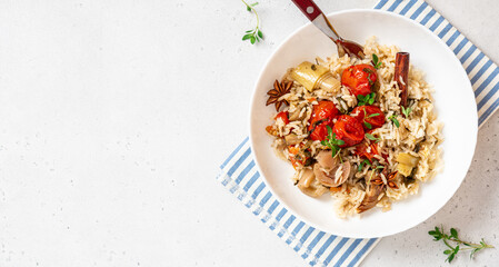 Spicy rice with vegetables. Stewed rice with cherry tomatoes, leek, herbs, and spices in a white bowl on a gray concrete background top view. Vegan food, Mediterranean cuisine. Free space for text.