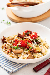 Spicy rice with vegetables. Stewed rice with cherry tomatoes, leek, herbs, and spices in a white bowl on a gray concrete background. Vegan food, Mediterranean cuisine.