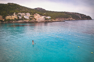 Aerial shot of woman paddling on paddle board on crystal clear turquoise water