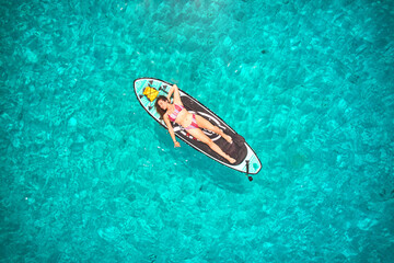 Aerial shot of woman laying on paddle board with a crystal clear turquoise water background