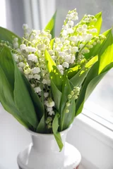 Poster Bouquet of fresh lily of the valley flowers on windowsill in sunlight, close up. © Gioia