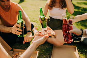 Friends drink beer and alcohol and eat pizza outdoors, hands close-up
