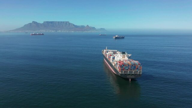 A large container ship for transporting goods near the port of Capetown, South Africa. A container ship carries cargo across the ocean. Transportation. Delivery. Logistics. Aerial 4K shot.