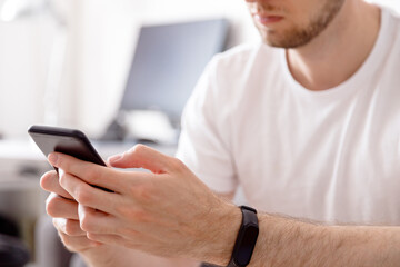 Young man in white shirt using mobile phone while sitting on sofa at home, modern design interior.