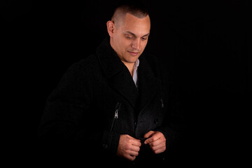 Fototapeta premium a young handsome man wears a black coat on a black background