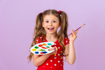 A joyful little girl with a paint palette and a brush on a purple background.