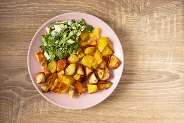Fried potatoes with salad on wooden background