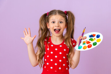 A little girl holds a paint palette in her hands and is very happy.