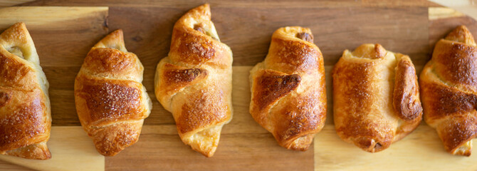 croissant, homemade fresh baked goods lies on a beautiful bamboo board on a wooden table, close up, flat lay, banner