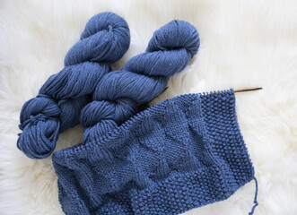 Fototapeta na wymiar Blue wool knitting blanket in progress with yarn hank and needles
