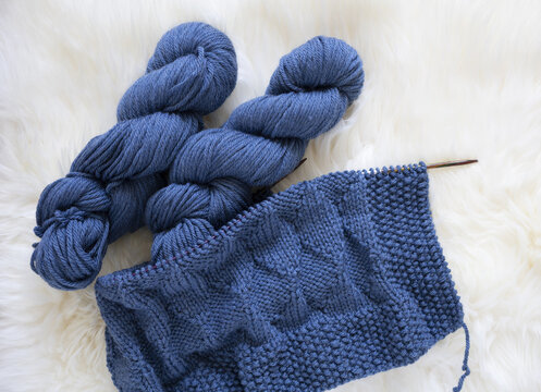Blue wool knitting blanket in progress with yarn hank and needles