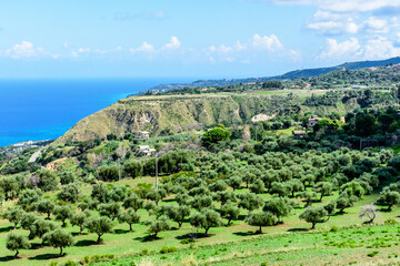 A view of a plateau high above the Mediterranean sea, surrounded by green olive groves and blue...