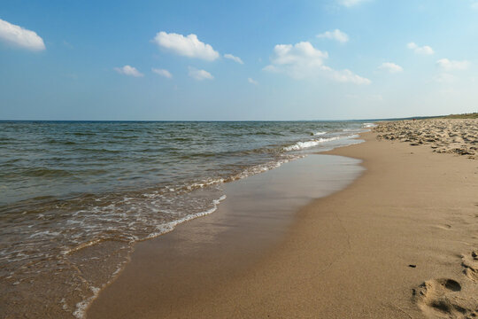 The coastal line of a sandy beach by the Baltic Sea on Sobieszewo island, Poland. The sea is gently waving. A bit of overcast. Solitude and serenity