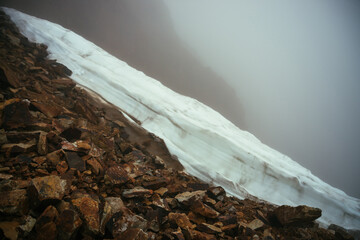 Gloomy minimalist foggy mountain landscape with snow cornice over abyss inside cloud. Above snow...