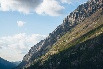 Beautiful mountain landscape with high green mountainside with sharp rocks in sunlight. Atmospheric mountain scenery with trees on steep slope in sunshine. Awesome sunny view to great rocky mountain.