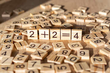 Scattered wooden plaques with numbers and signs. Two by two is four. Teaching material in mathematics, Montessori method. School background. Simple solving concept. Laser cutting and printing on wood.