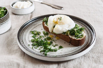 Healthy Breakfast with Poached Egg on toast with cream cheese and chopped mix of green onions, dill and parsley on greige linen tablecloth