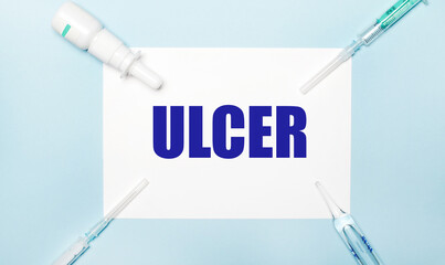 On a light blue background, syringes, a medicine bottle, an ampoule and a white sheet of paper with...