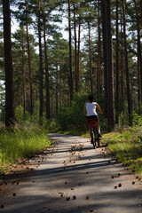 Obraz premium A young woman with short black hair rides a bicycle on a beautiful day entering a pine forest in Germany, back view