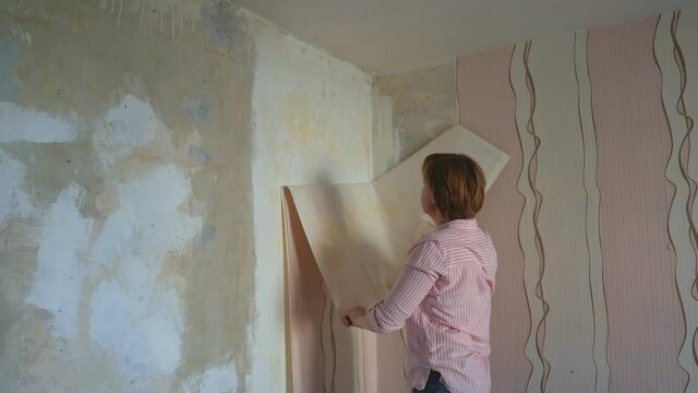 Woman removes old wallpaper from the wall. Preparing the walls for pasting new wallpaper. Repairs in house and apartment