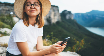 happy blonde tourist woman in glasses and summer hat using internet on cellphone and relax on...