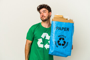 Young caucasian man man recycling cardboard isolated on white background dreaming of achieving...