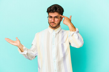 Young caucasian man isolated on blue background holding and showing a product on hand.