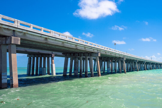 Highway concrete bridge across turquoise ocean water in Florida. Green water, concrete pilots, blue sky with soft clouds and speed limit sign. Driving across the sea in tropical paradise