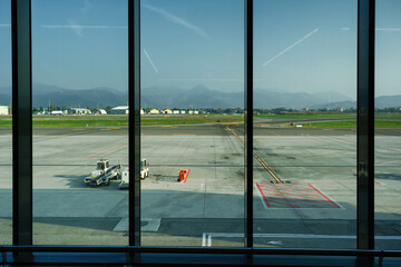 View through the airport departure terminal window to the runway, town buildings and misty mountains near the horizon