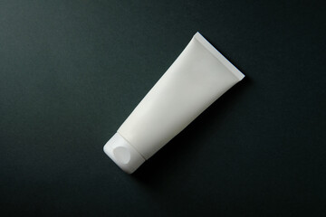 White tube with cream on a dark background, place for an inscription, top view