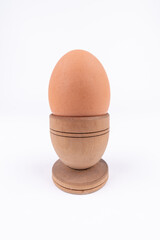 Vertical shot of hen egg in old wooden egg stand isolated on white background. Conceptual art for egg-related foods. Breakfast minimalistic concept.