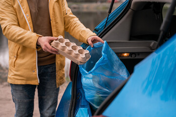 cropped view of man holding carton container near blue trash bag in car - Powered by Adobe